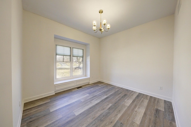 empty room with visible vents, wood finished floors, baseboards, and a chandelier