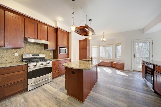 kitchen featuring beverage cooler, under cabinet range hood, a sink, tasteful backsplash, and appliances with stainless steel finishes