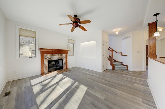 unfurnished living room with stairway, light wood-style flooring, a brick fireplace, and visible vents