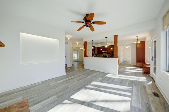 unfurnished living room with visible vents, baseboards, arched walkways, light wood-style floors, and ceiling fan with notable chandelier