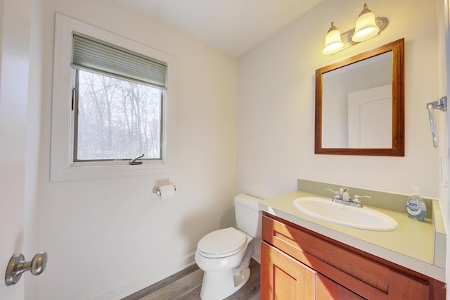 half bath featuring toilet, vanity, baseboards, and wood finished floors