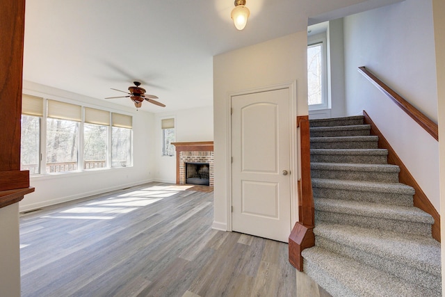 staircase with a wealth of natural light, a brick fireplace, baseboards, and wood finished floors