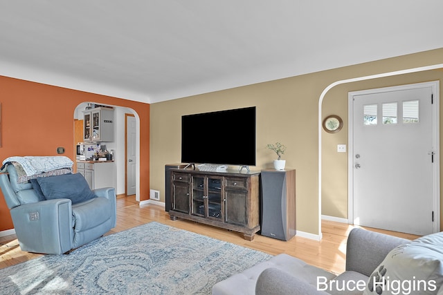 living area featuring baseboards, arched walkways, and light wood finished floors