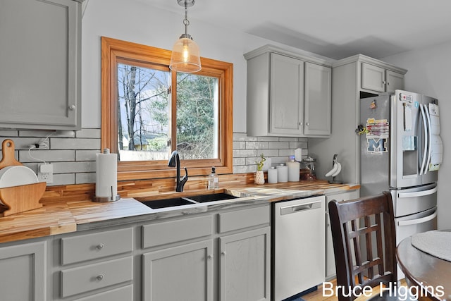 kitchen with a sink, stainless steel appliances, wood counters, decorative light fixtures, and backsplash