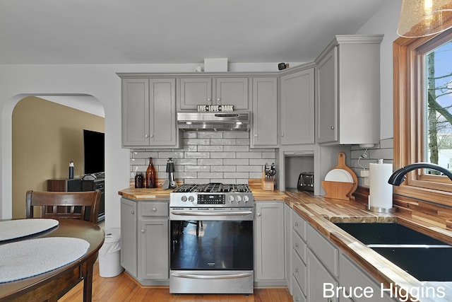 kitchen featuring arched walkways, a sink, wood counters, stainless steel gas range oven, and exhaust hood