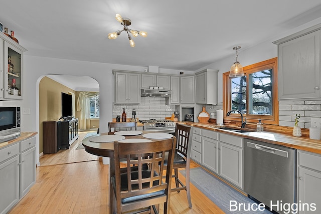 kitchen featuring under cabinet range hood, light wood-style flooring, appliances with stainless steel finishes, arched walkways, and a sink