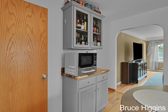 kitchen featuring arched walkways, light wood-style floors, glass insert cabinets, stainless steel microwave, and butcher block counters