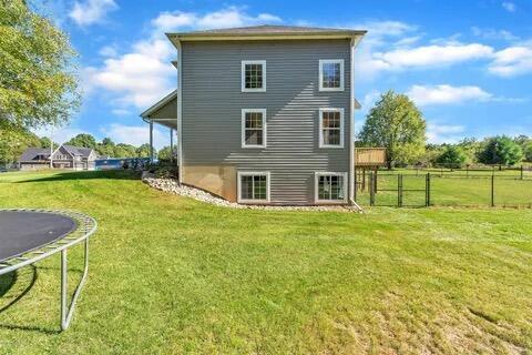 rear view of property with a trampoline, a lawn, and fence