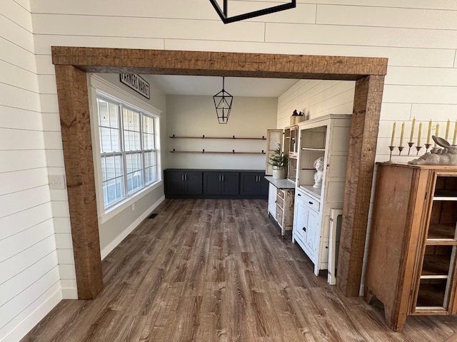 interior space with visible vents, dark wood-type flooring, decorative light fixtures, wood walls, and open shelves