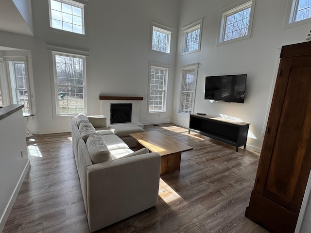 living room featuring dark wood finished floors, a fireplace, a high ceiling, and baseboards