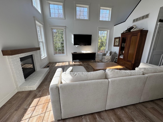 living area with dark wood-style floors, visible vents, baseboards, a fireplace, and a towering ceiling