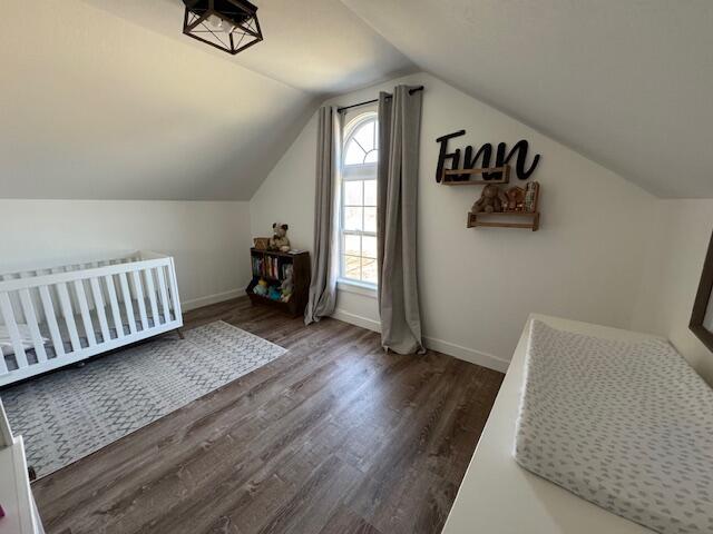 bedroom featuring lofted ceiling, baseboards, and dark wood-style flooring