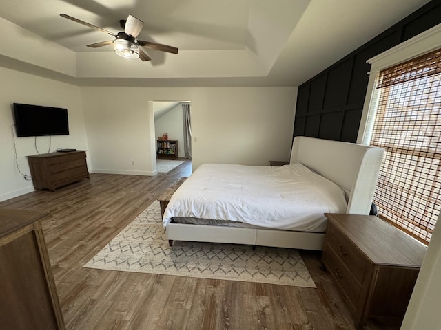 bedroom featuring baseboards, a ceiling fan, a tray ceiling, and wood finished floors