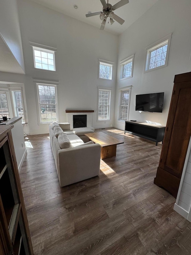 living room featuring a fireplace with raised hearth, dark wood-type flooring, a towering ceiling, and ceiling fan