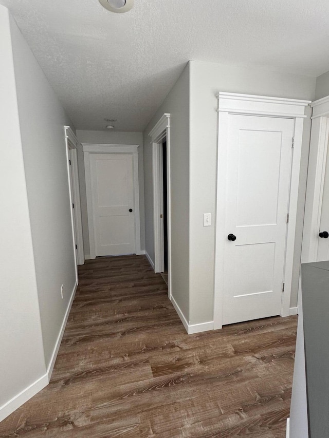 hallway with dark wood-style floors, a textured ceiling, and baseboards