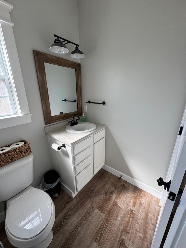 bathroom with toilet, vanity, baseboards, and wood finished floors