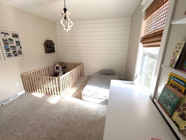 carpeted bedroom with visible vents, a crib, wooden walls, and baseboards