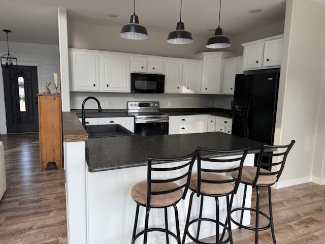 kitchen with black appliances, a sink, dark countertops, wood finished floors, and white cabinets