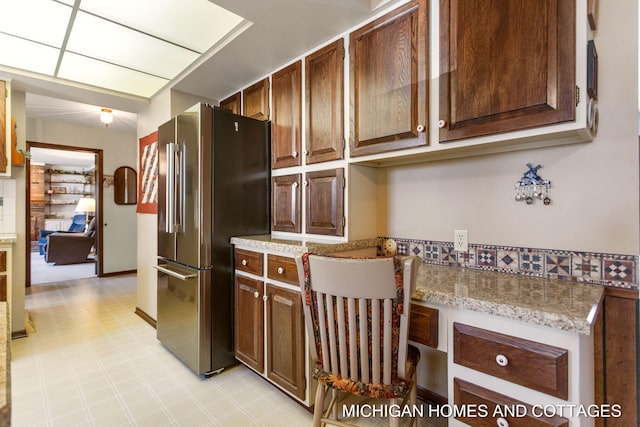 kitchen with built in desk, light floors, freestanding refrigerator, and light stone countertops