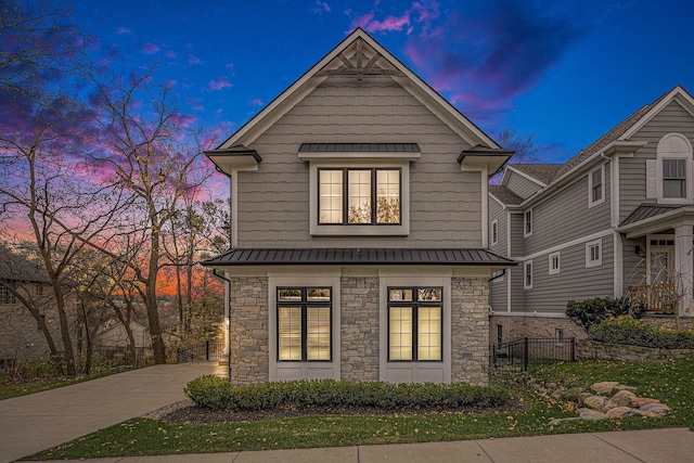 view of front of home featuring driveway, a standing seam roof, stone siding, fence, and metal roof