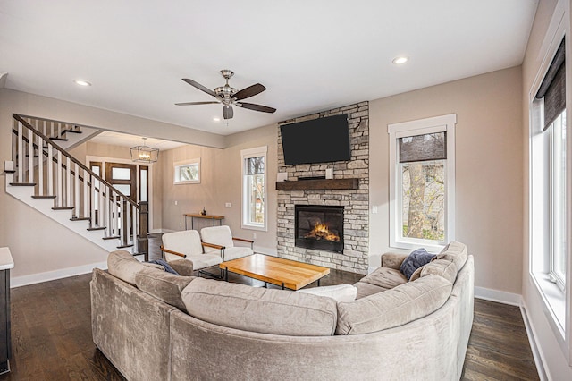 living room featuring dark wood-type flooring, a stone fireplace, stairs, and a healthy amount of sunlight