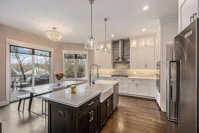 kitchen featuring a sink, dark wood-style floors, stainless steel appliances, wall chimney exhaust hood, and decorative backsplash