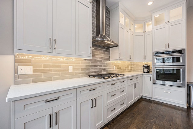 kitchen with dark wood-style flooring, stainless steel appliances, white cabinetry, wall chimney range hood, and tasteful backsplash