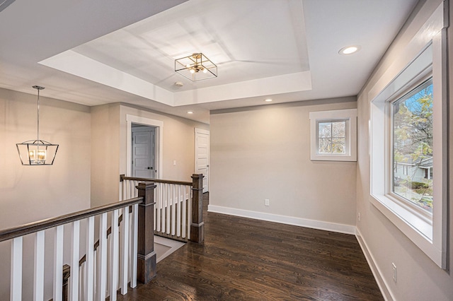 corridor featuring a raised ceiling, dark wood-style floors, an upstairs landing, and baseboards