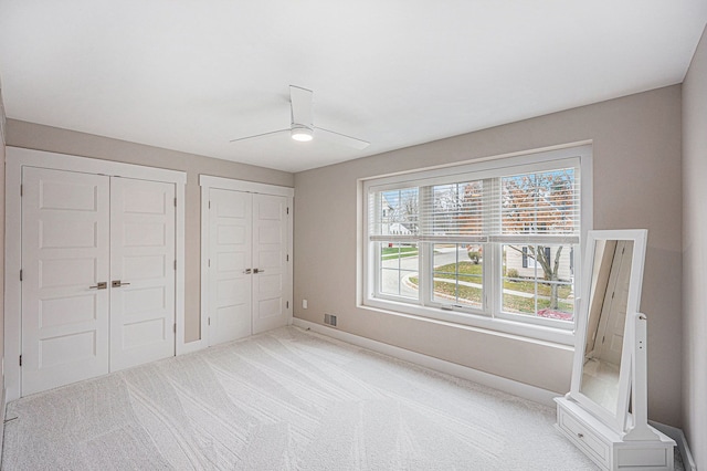 unfurnished bedroom featuring a ceiling fan, baseboards, visible vents, carpet floors, and two closets