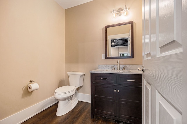 half bath featuring toilet, vanity, baseboards, and wood finished floors