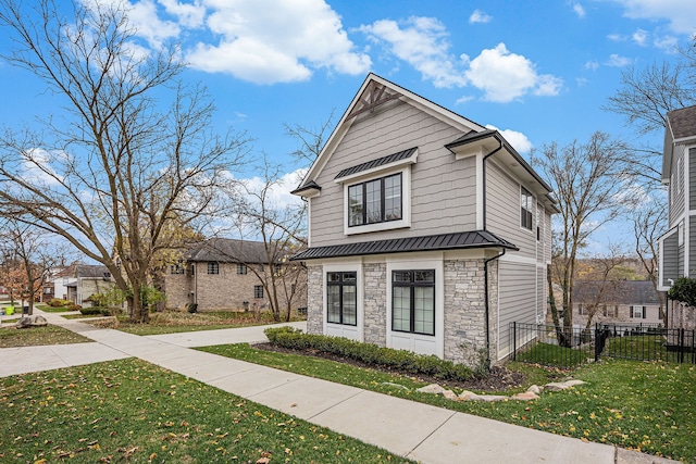 view of front facade featuring fence, a standing seam roof, a front lawn, stone siding, and metal roof