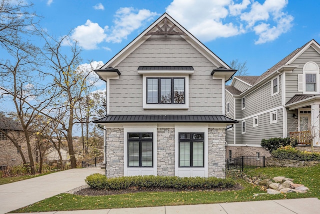 view of front facade featuring a standing seam roof, stone siding, fence, concrete driveway, and metal roof