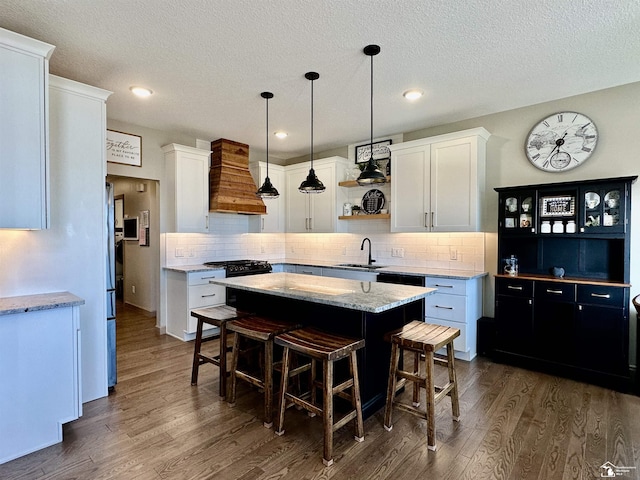 kitchen featuring open shelves, a sink, a center island, custom exhaust hood, and dark wood-style flooring