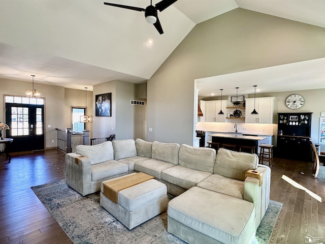 living room with ceiling fan with notable chandelier, dark wood-style floors, visible vents, and high vaulted ceiling