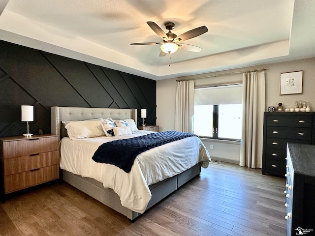 bedroom with a ceiling fan, a tray ceiling, and wood finished floors