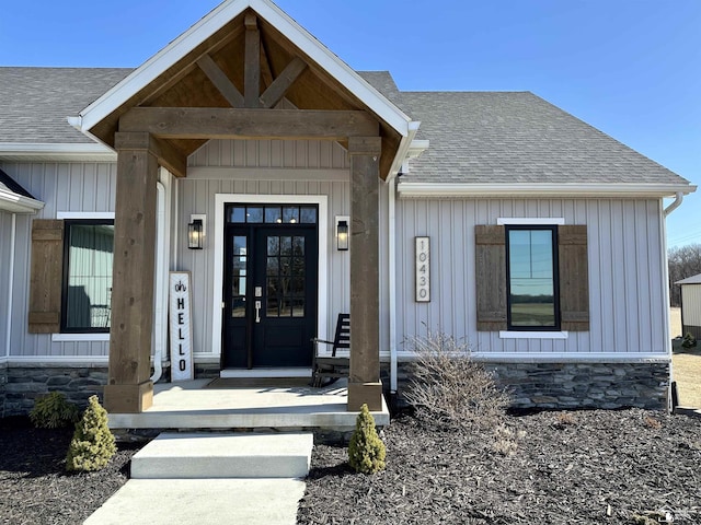 doorway to property with a porch, stone siding, board and batten siding, and a shingled roof