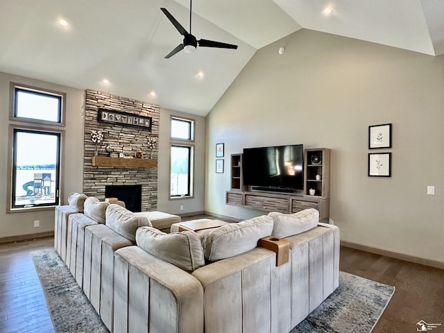 living room with high vaulted ceiling, a ceiling fan, light wood-style floors, a stone fireplace, and baseboards