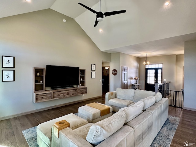 living area with dark wood-style floors, ceiling fan with notable chandelier, high vaulted ceiling, and baseboards