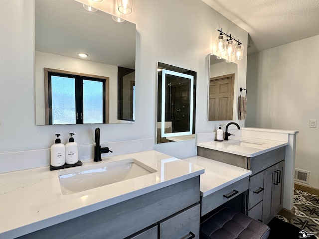 full bathroom featuring a textured ceiling, two vanities, tiled shower, and a sink