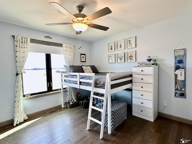 bedroom with a textured ceiling, wood finished floors, visible vents, and baseboards