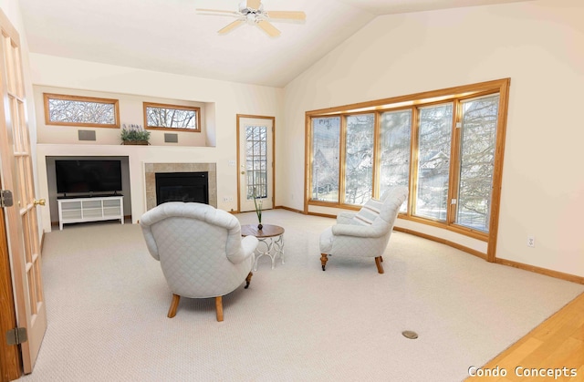 living area featuring a ceiling fan, a tiled fireplace, carpet floors, baseboards, and vaulted ceiling