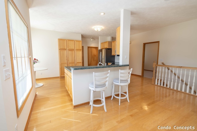 kitchen with light wood-type flooring, dark countertops, light brown cabinets, and freestanding refrigerator