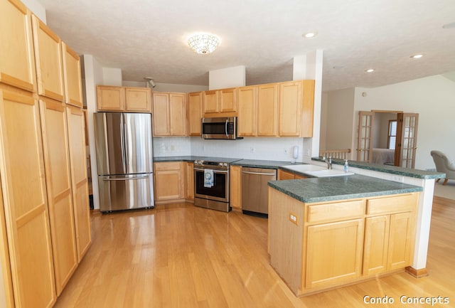 kitchen with light brown cabinets, a peninsula, light wood-style floors, stainless steel appliances, and a sink