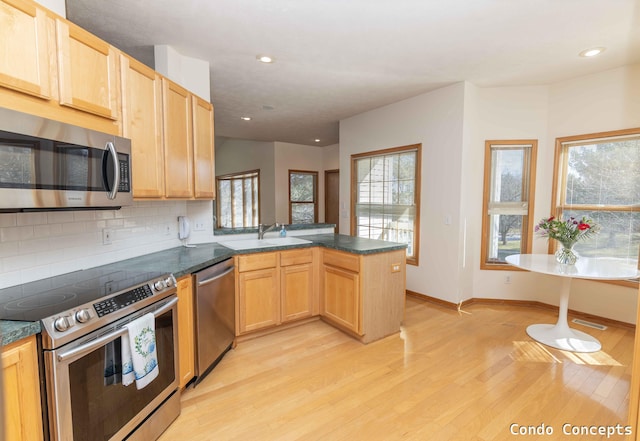 kitchen with decorative backsplash, light wood-style flooring, a peninsula, stainless steel appliances, and a sink