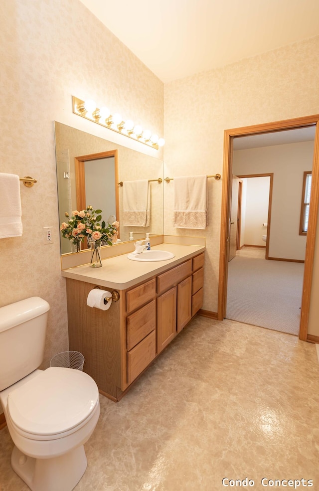 bathroom with baseboards, toilet, vanity, and wallpapered walls