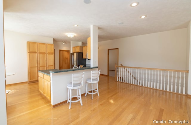 kitchen featuring dark countertops, a breakfast bar area, light wood finished floors, and freestanding refrigerator