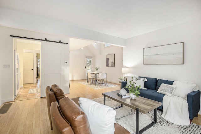 living area with a barn door, light wood-style floors, and baseboards