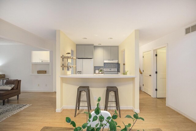 kitchen featuring a kitchen bar, under cabinet range hood, electric range oven, light wood-style floors, and white fridge with ice dispenser