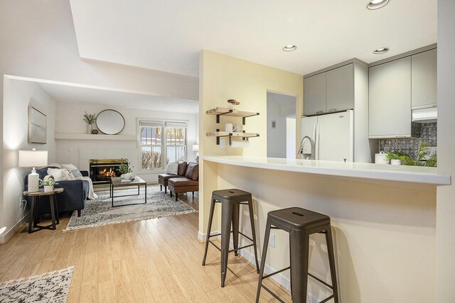 kitchen with light wood finished floors, gray cabinetry, a kitchen bar, a fireplace, and freestanding refrigerator