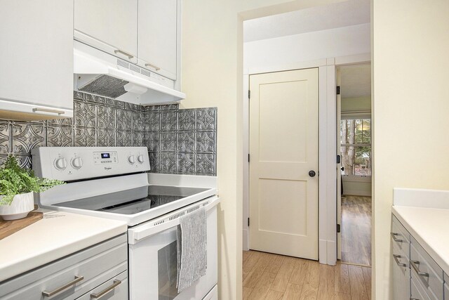 kitchen with light wood finished floors, white range with electric cooktop, light countertops, under cabinet range hood, and tasteful backsplash